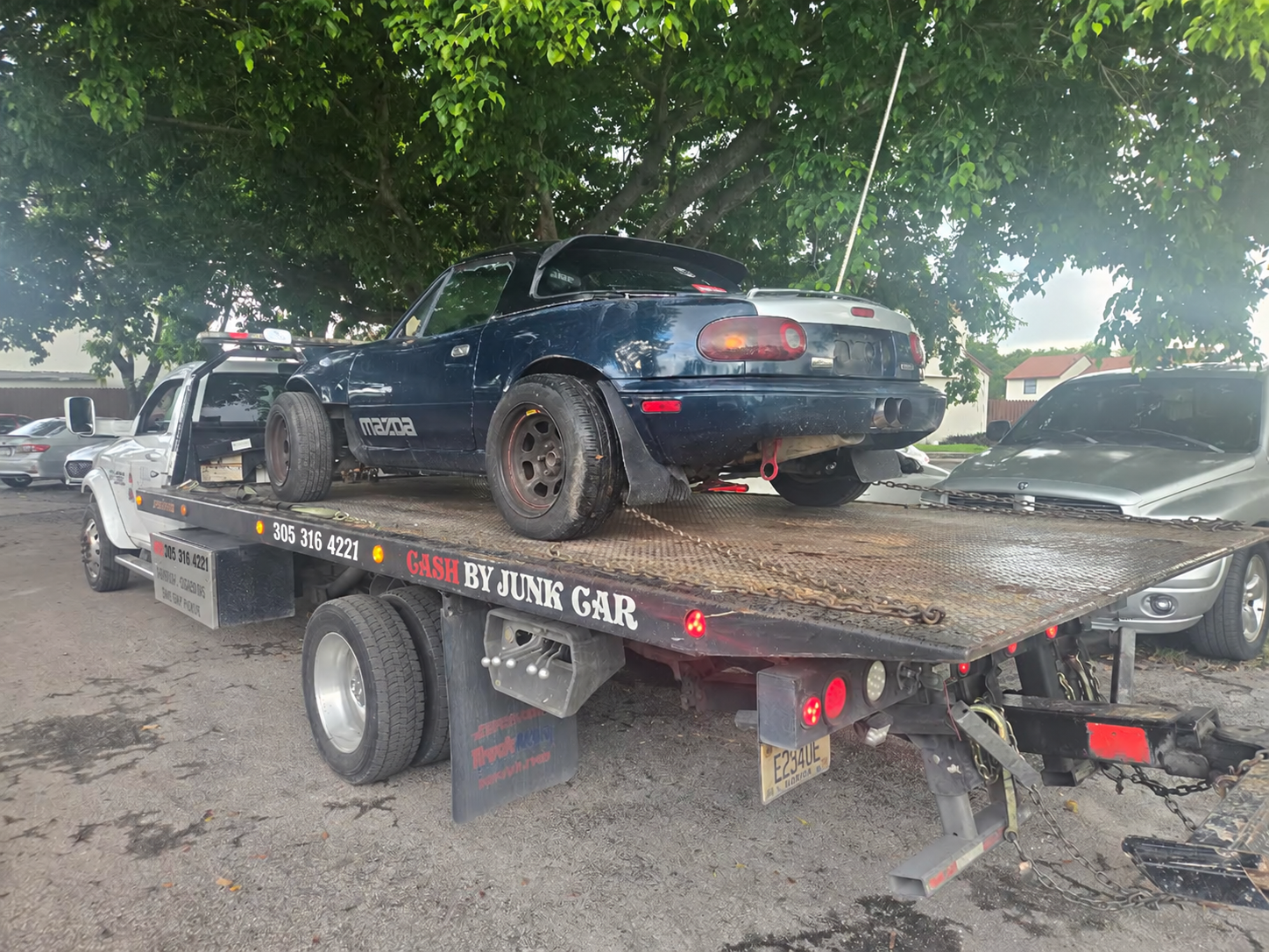 Rear view of a Mazda convertible secured on a flatbed tow truck