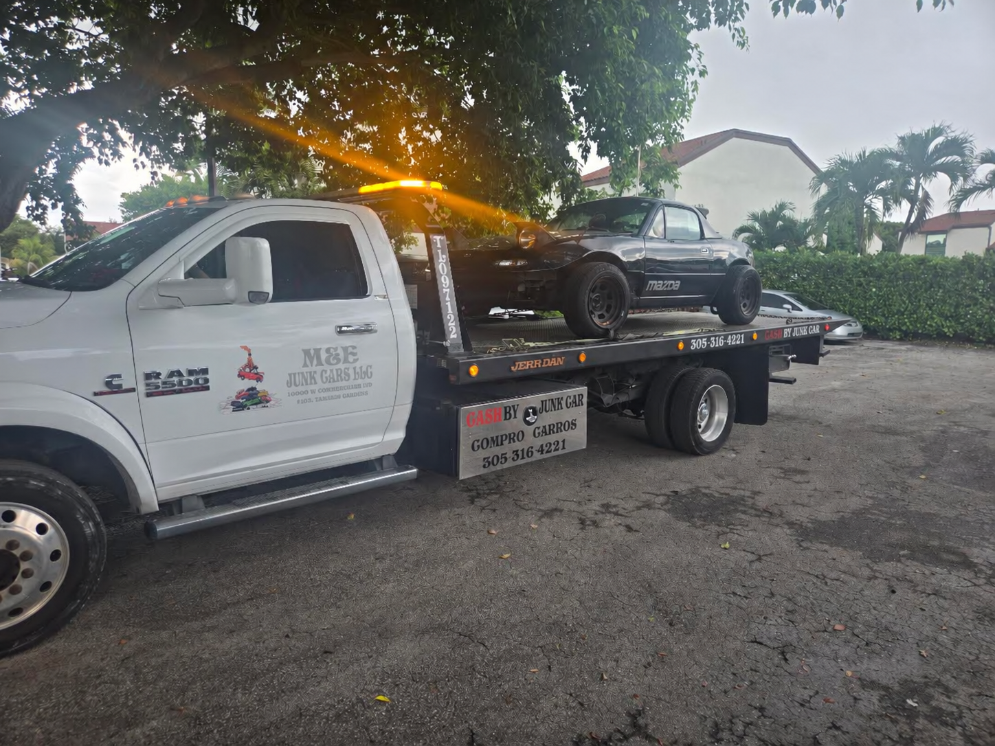 White flatbed tow truck carrying a dark Mazda convertible in Miami